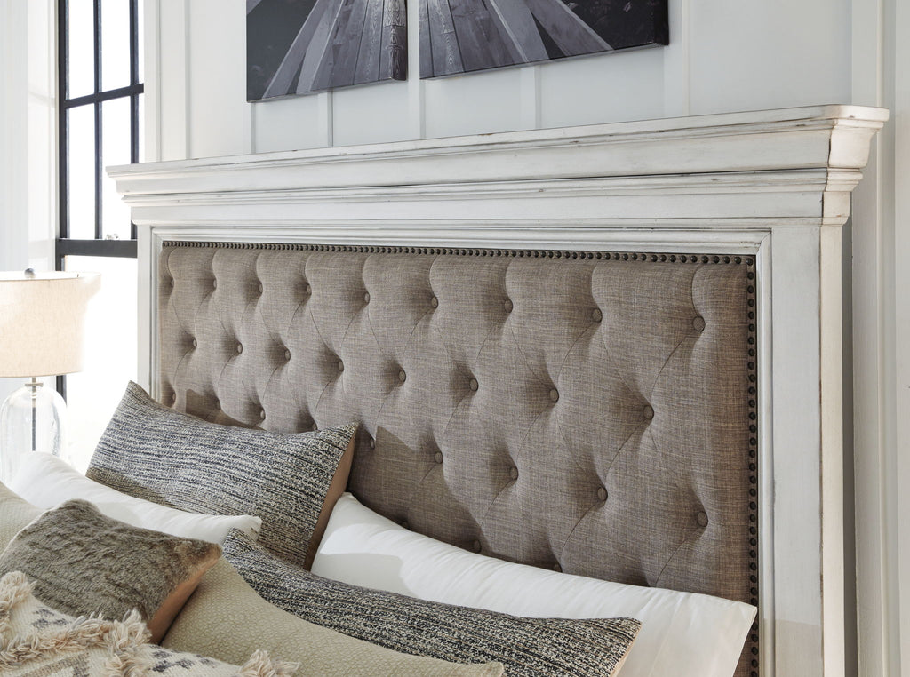 Tufted taupe upholstered headboard with nailhead trim and pillows