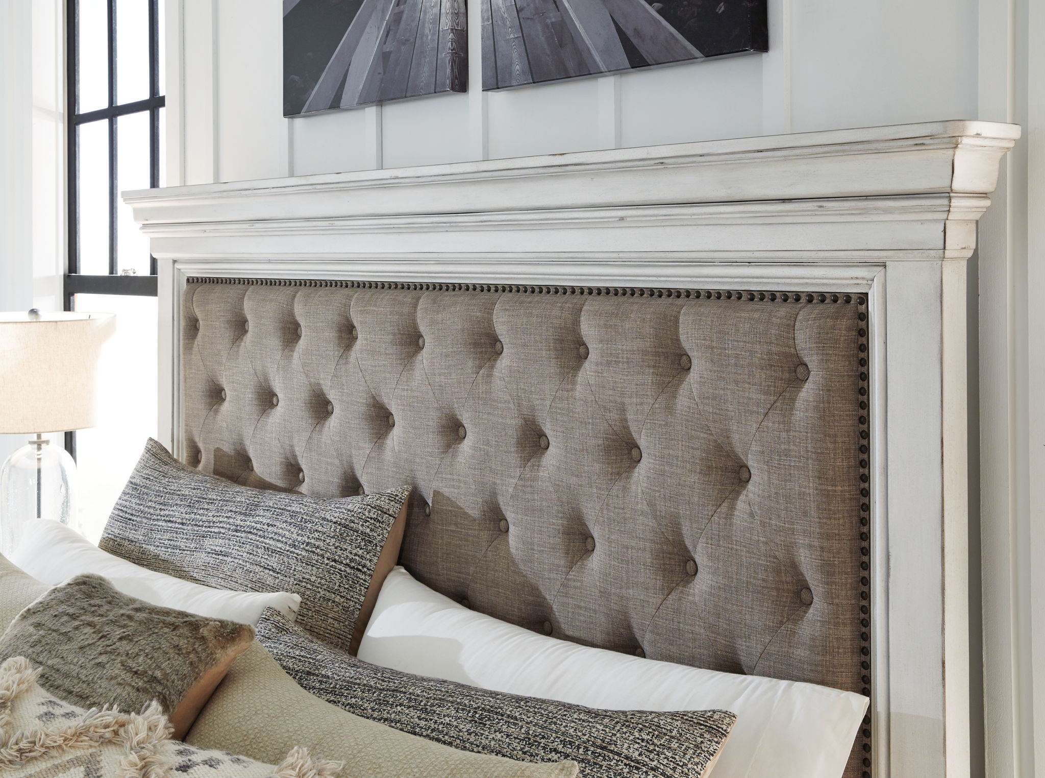 Tufted taupe upholstered headboard with nailhead trim and pillows
