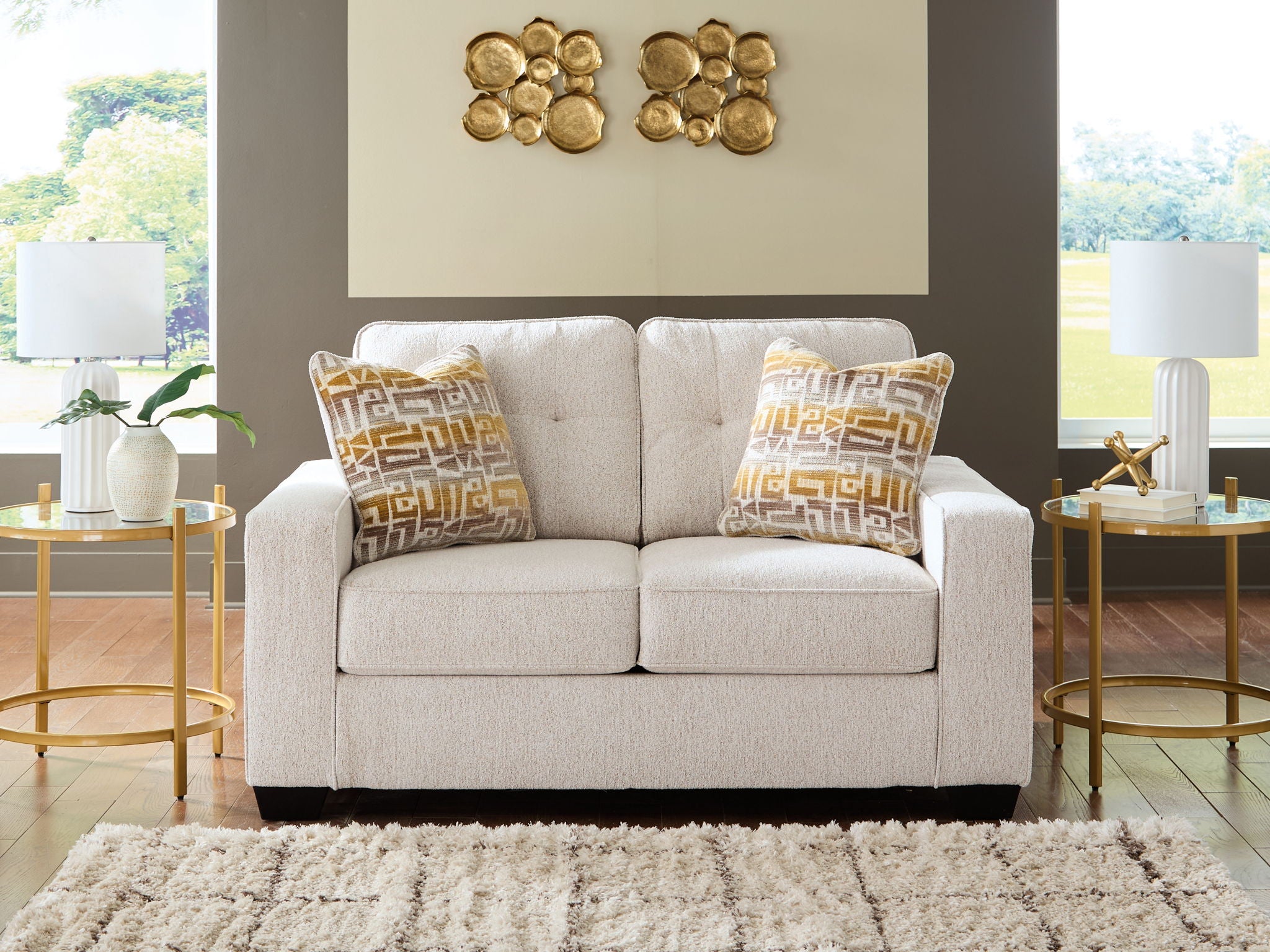 Light gray upholstered loveseat with two square patterned throw pillows in gold and beige