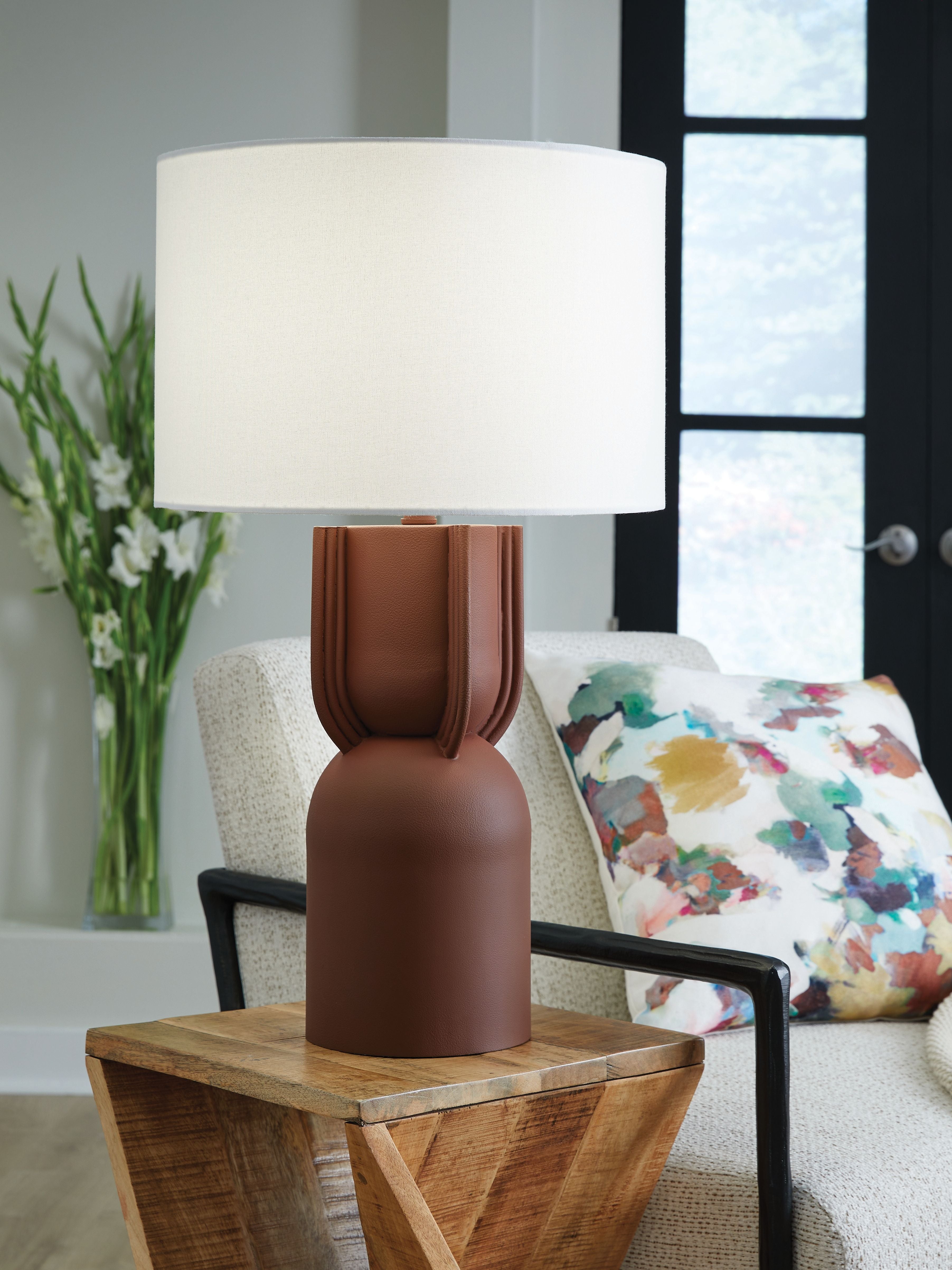 Brick-red metal table lamp with white drum shade on wooden side table