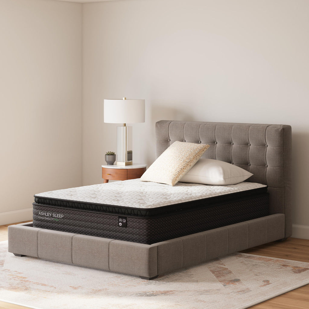 White-topped mattress on dark gray upholstered bed frame with two pillows