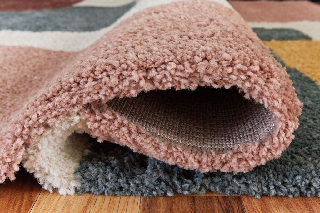 Pink shag-style rug edge with curled pile and gray backing