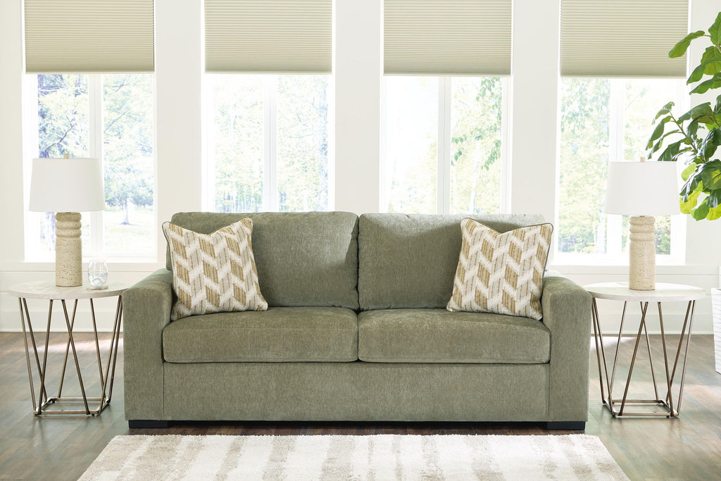 Green and gray upholstered sofa with two patterned pillows in a living room setting