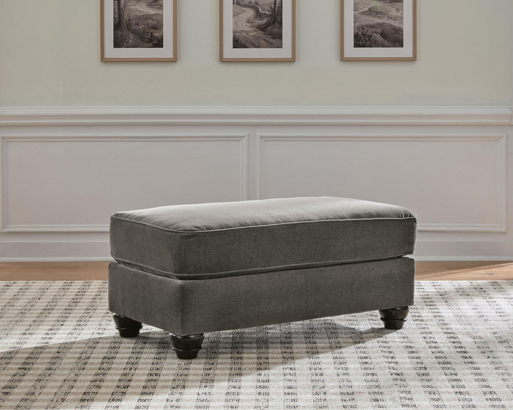 Gray upholstered ottoman with padded top and dark wood tapered legs.