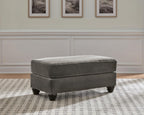 Gray upholstered ottoman with padded top and dark wood tapered legs.