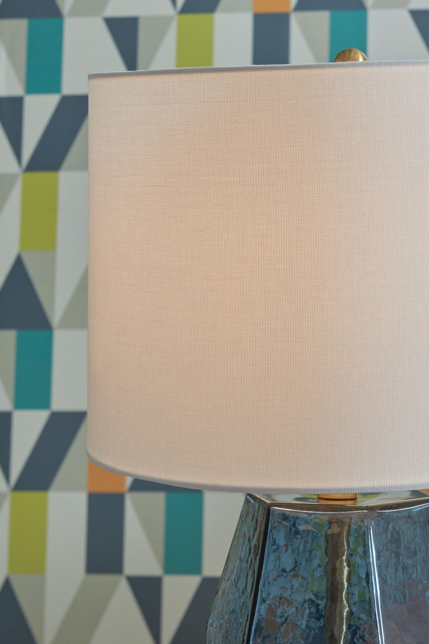 White drum lamp shade over blue faceted glass base with brass top detail