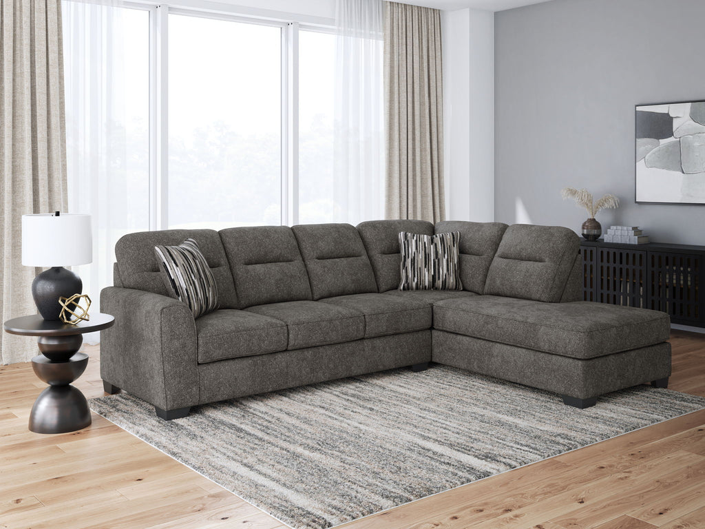 Dark gray sectional sofa with chaise, tufted back cushions, and striped pillows on the corner arm