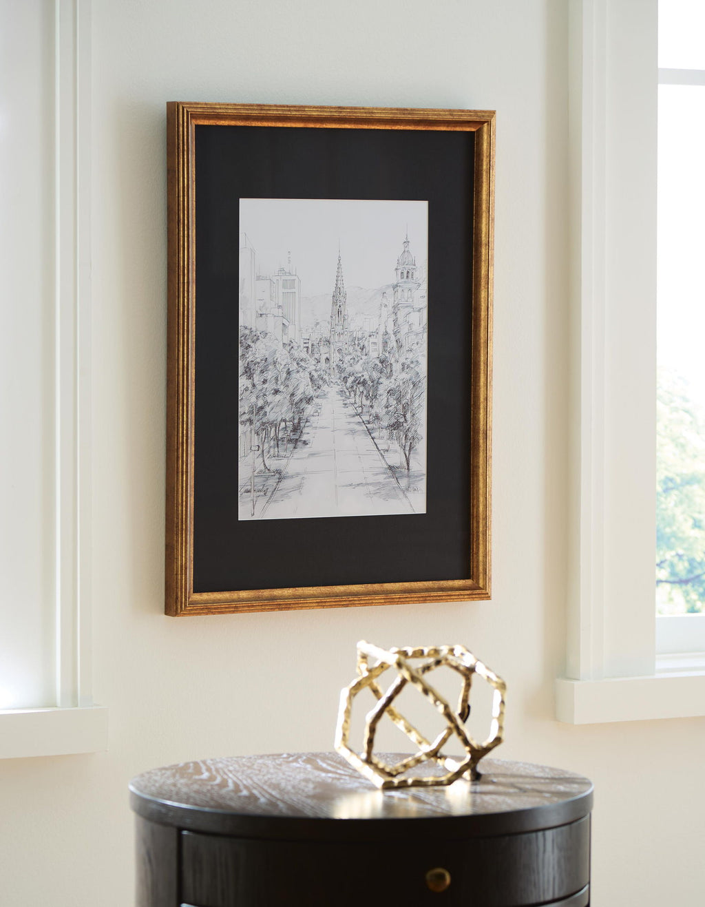 Gold-framed black-and-white cityscape print on wall above a dark round table