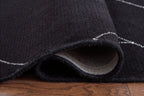Black rug corner showing folded edge, underside backing, and white stitch trim