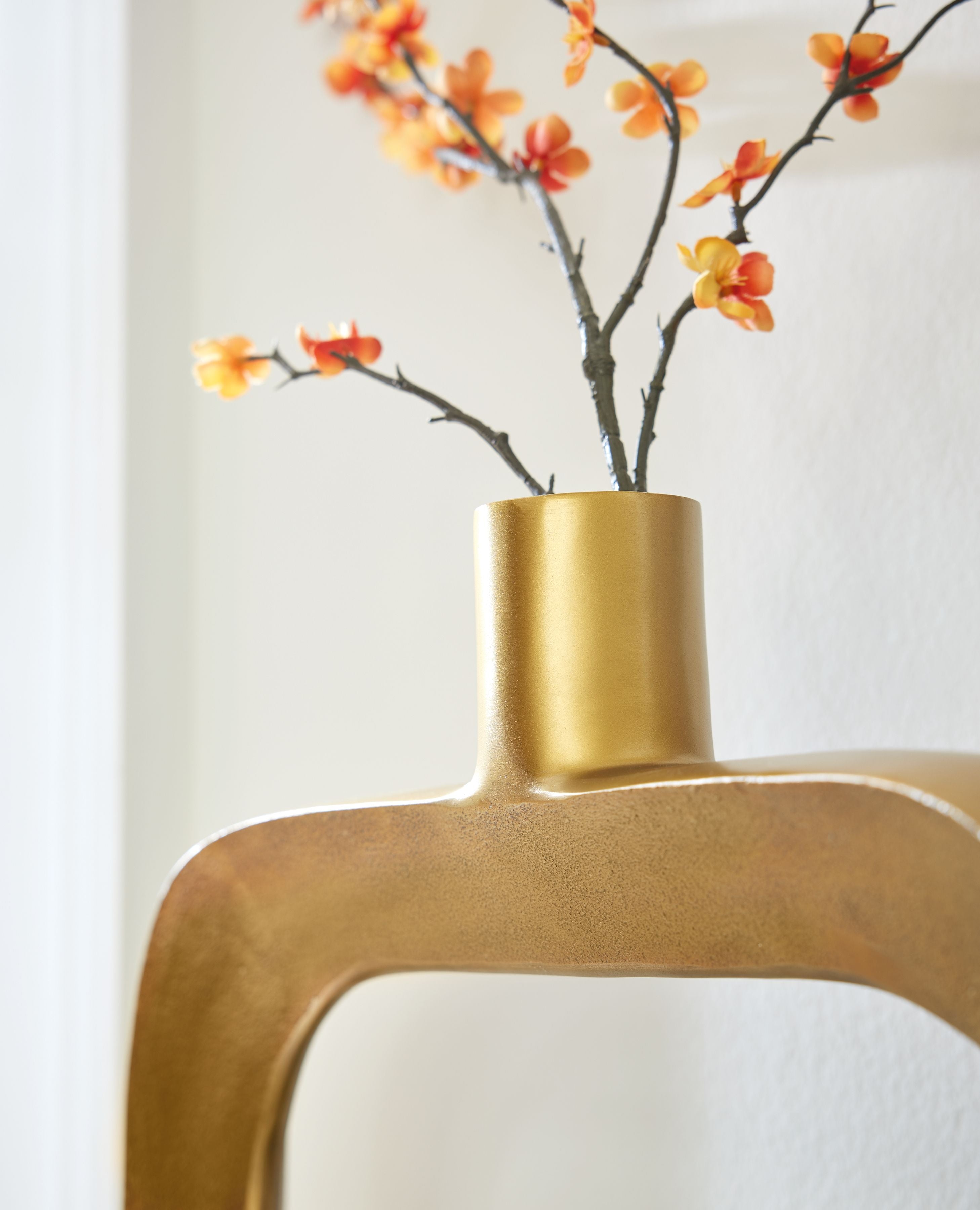 Gold vase with cylindrical neck and oval opening, holding orange blossoms