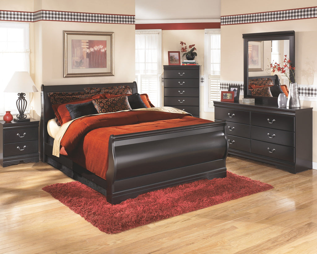 Black sleigh bed with red-orange comforter and patterned throw pillows