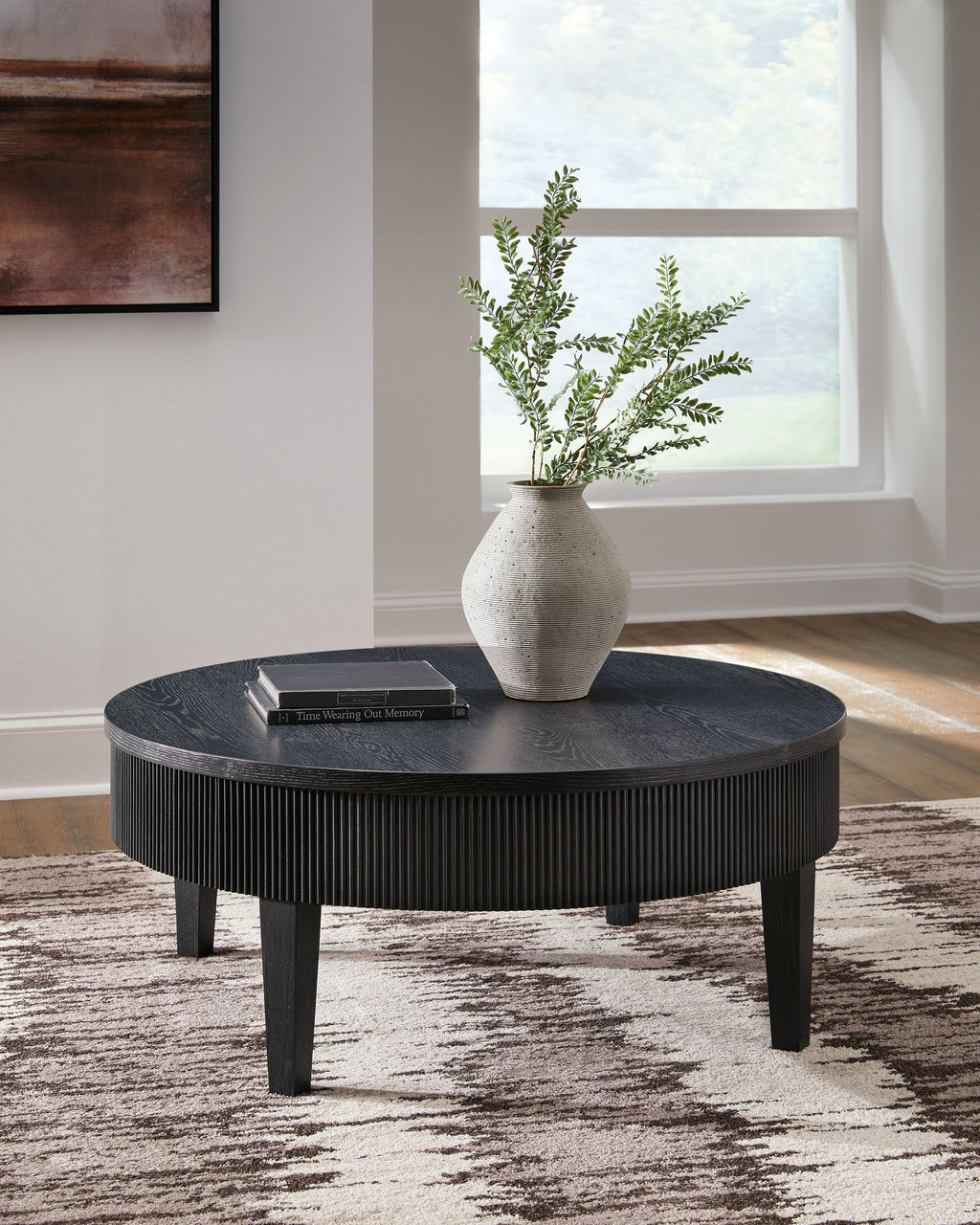 Black round cocktail table with ribbed sides, dark legs, and items on top