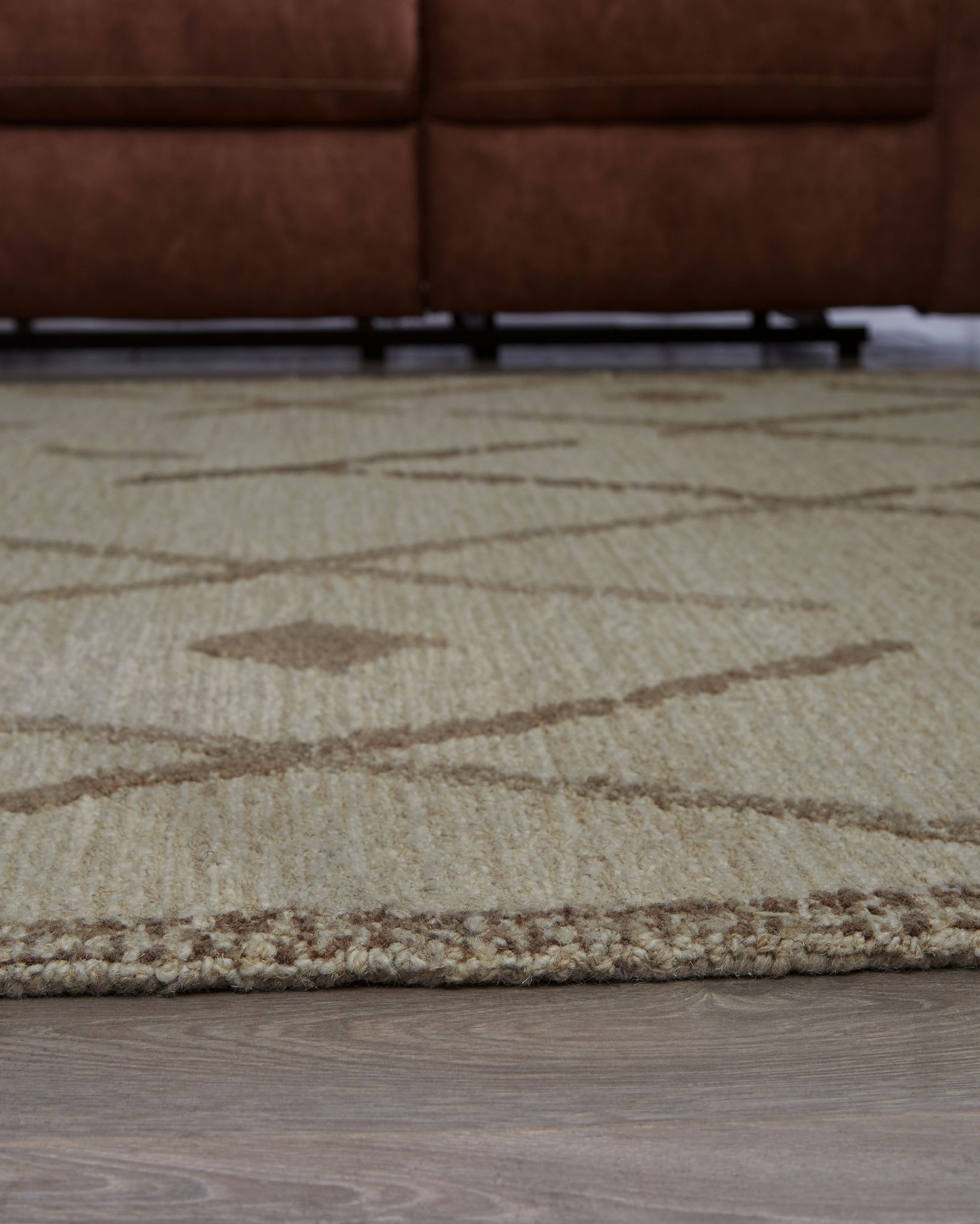 Beige rug close-up with brown swoosh lines and X/diamond geometric pattern.