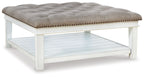 Tufted ottoman cocktail table in light beige, whitewash legs, nailhead trim, shelf