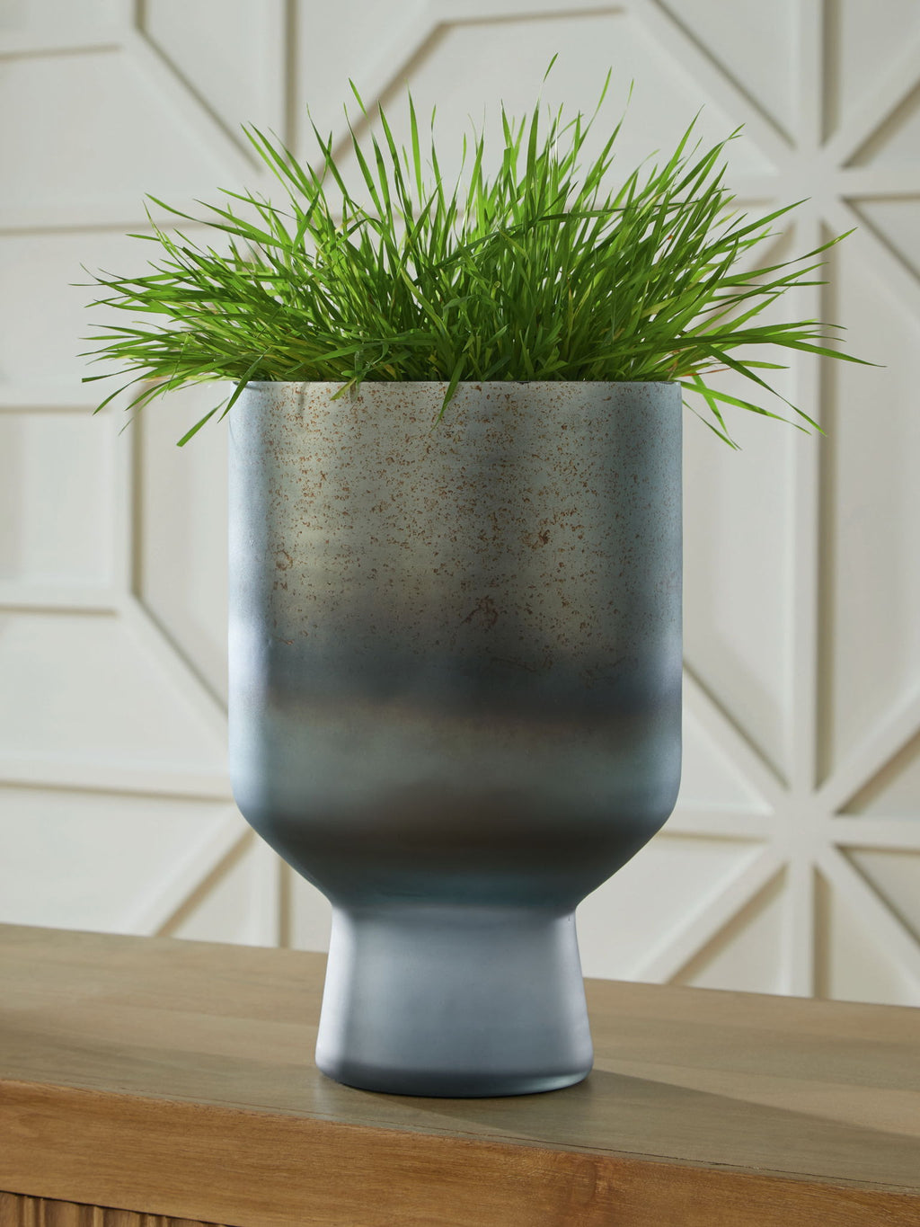 Blue speckled vase holding green grass, with flared rim and pedestal base.
