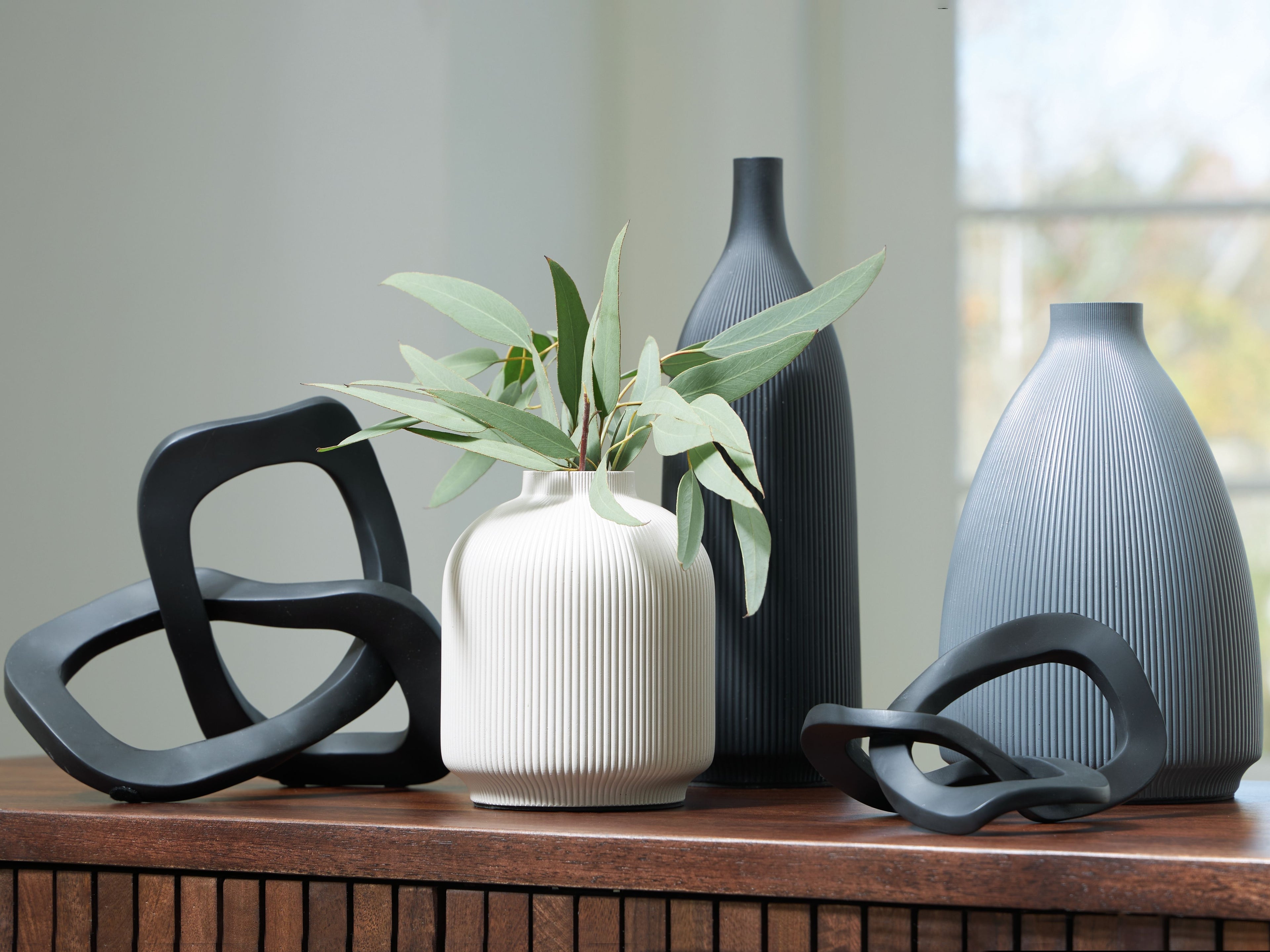 Ribbed ceramic vases with black loop accents, including a white vase with stems