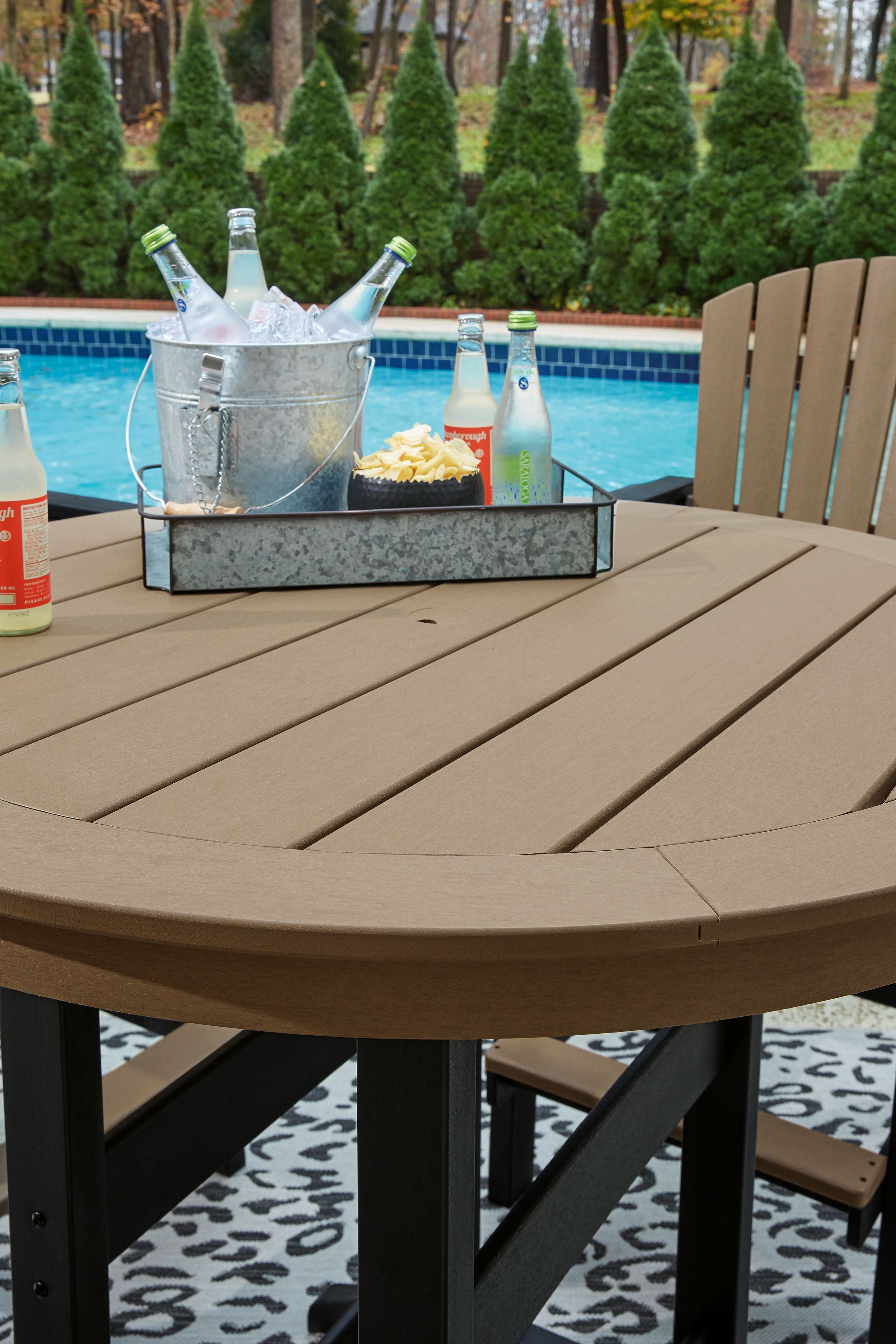 Round outdoor dining table with driftwood top and black base, water bottles and tray