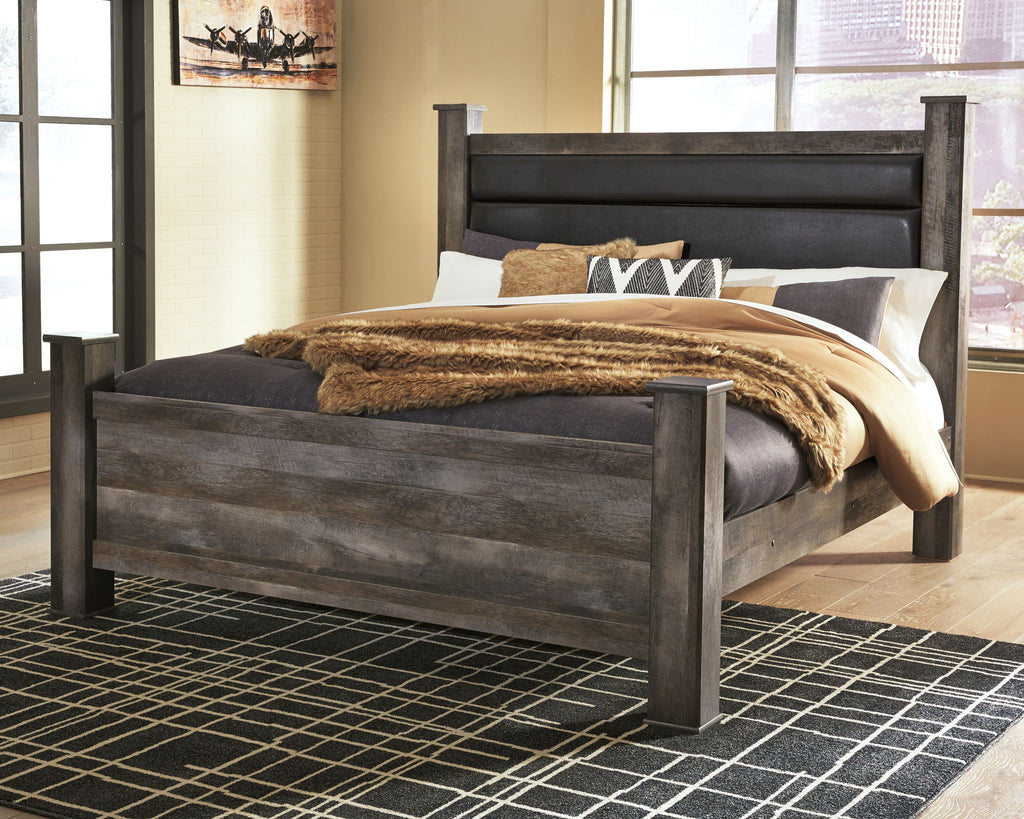 Gray poster bed with tall upholstered headboard and draped knit throw across mattress
