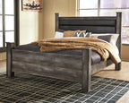 Gray poster bed with tall upholstered headboard and draped knit throw across mattress