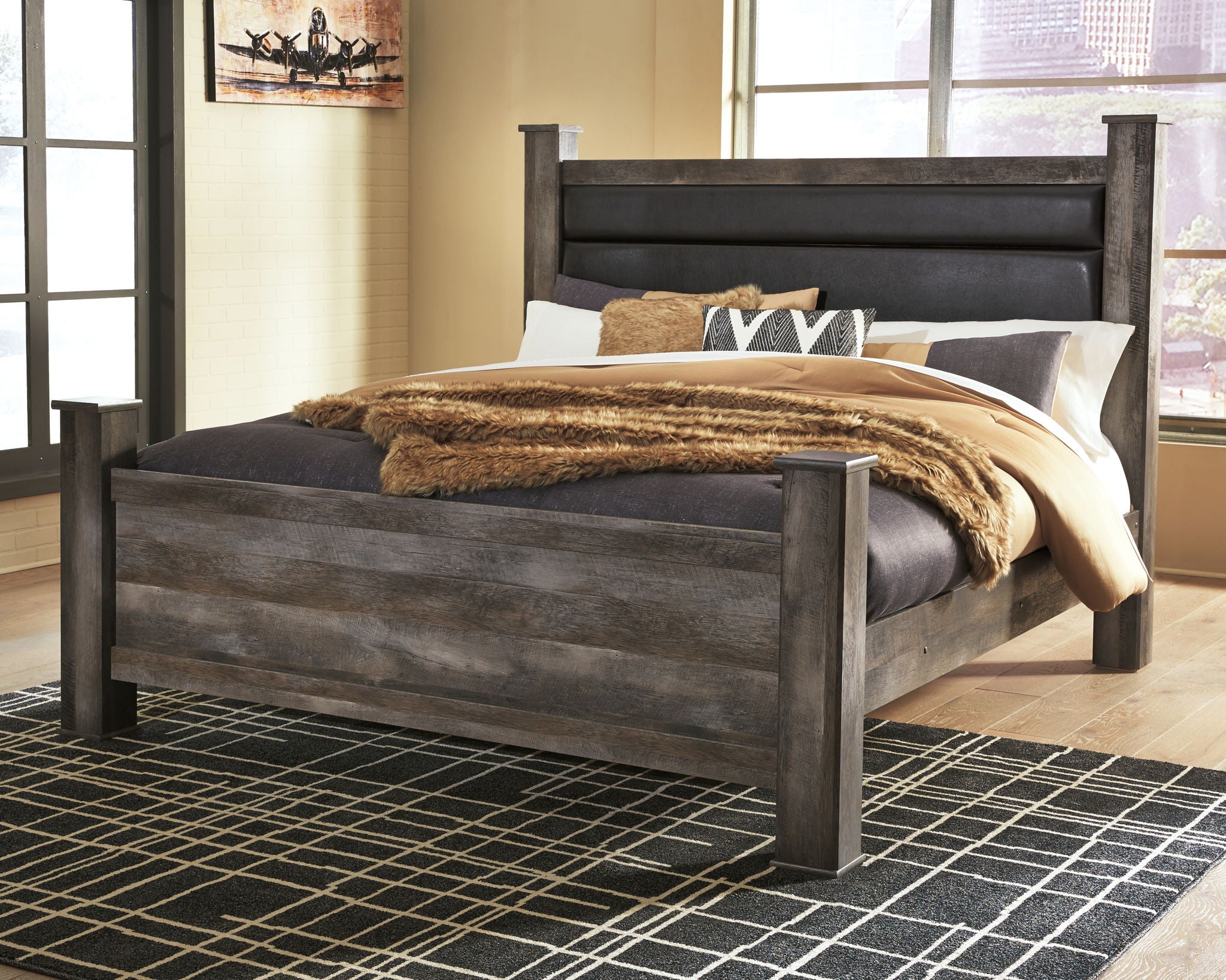 Gray poster bed with tall upholstered headboard and draped knit throw across mattress
