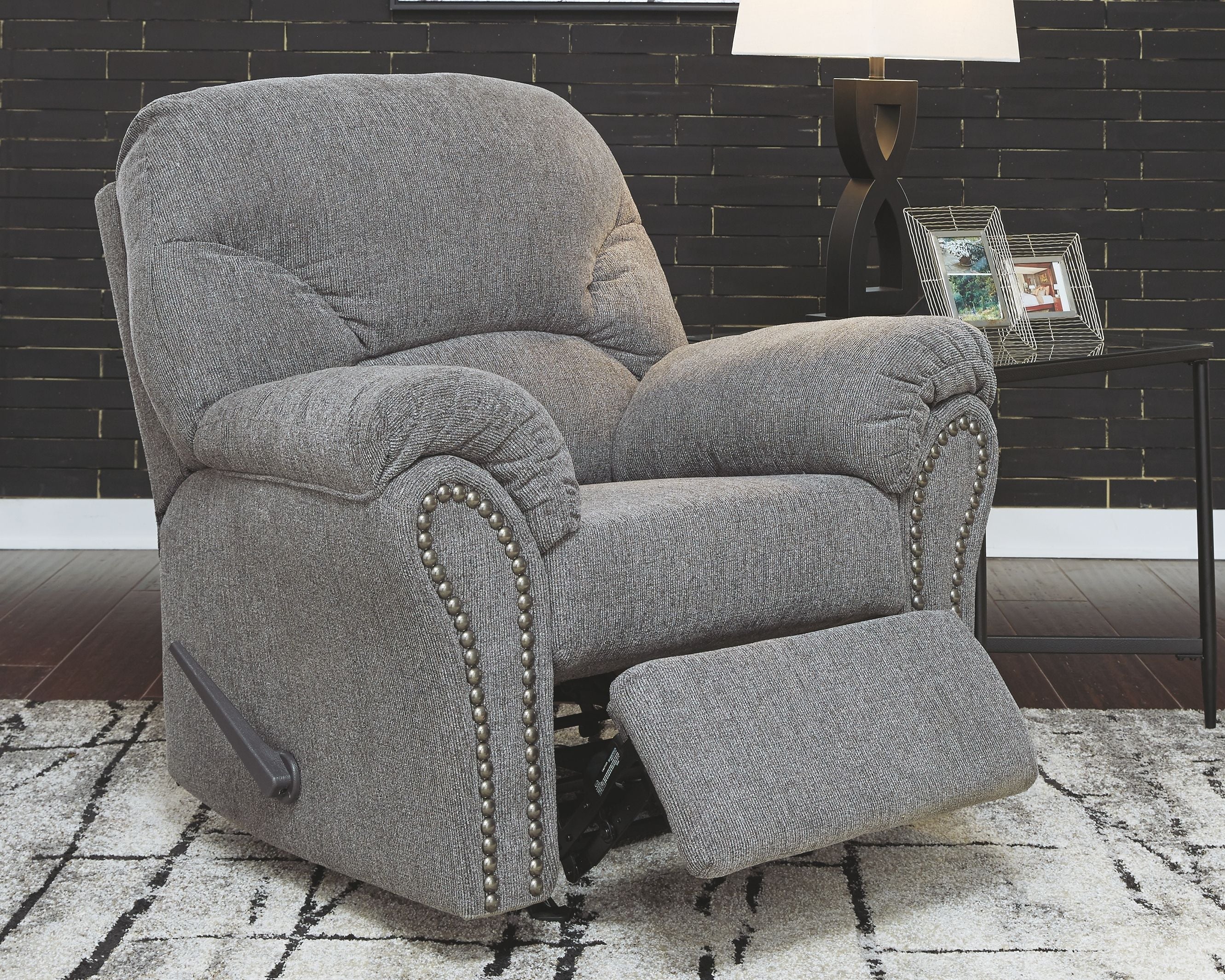 Dark gray recliner chair with padded armrests, tufted back, and studded trim