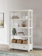 Antique white bookcase with open shelving and lower drawer for display items.