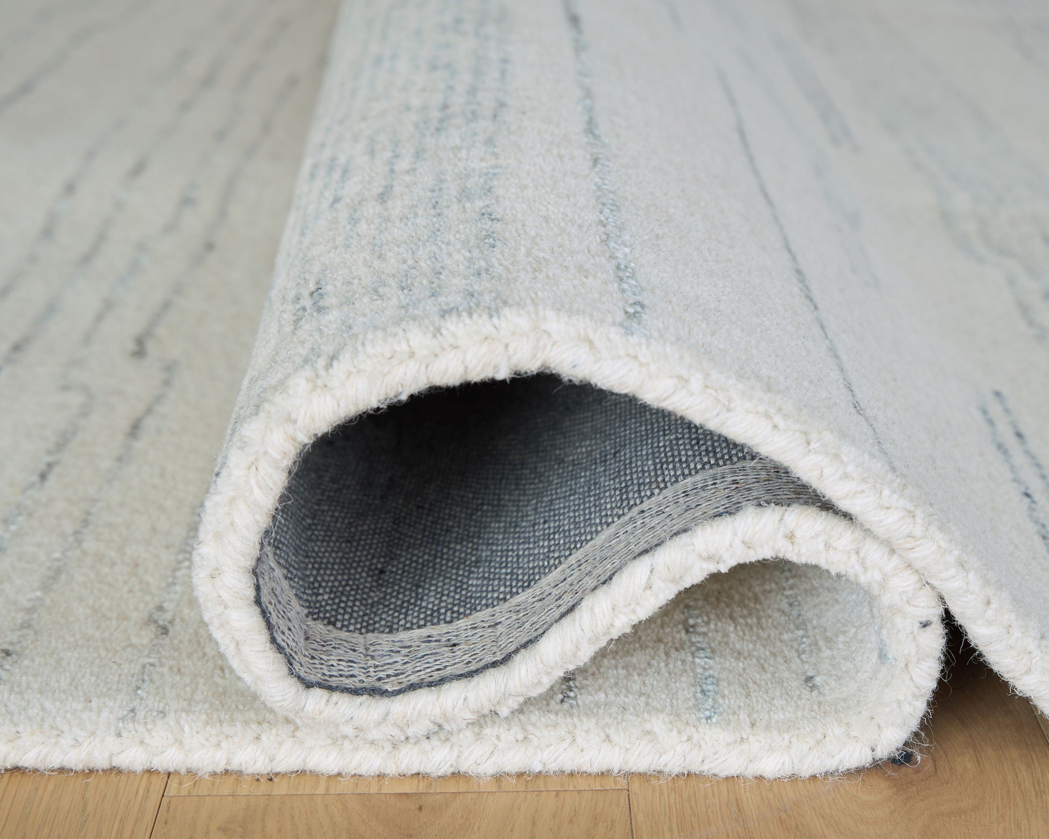 Rolled light blue and white rug edge with stitched backing and textured pile