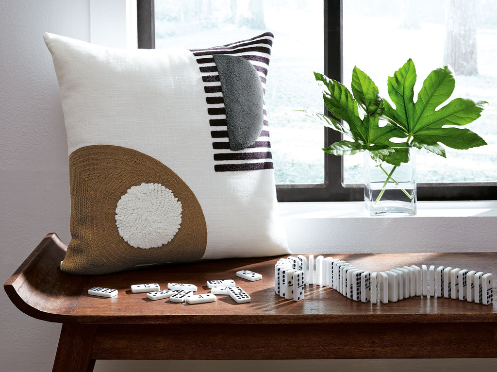 White throw pillow with brown circular applique and black-and-white striped accent