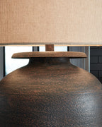 Antique brown metal lamp base with circular top and beige drum shade
