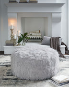 Oversized ottoman with shaggy light gray faux fur upholstery and rounded silhouette