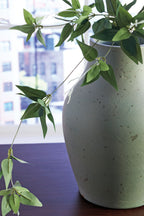 Green ceramic vase with dangling stems and leaves