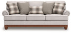 Light gray sofa with plaid pillows, tufted arms, and wooden legs