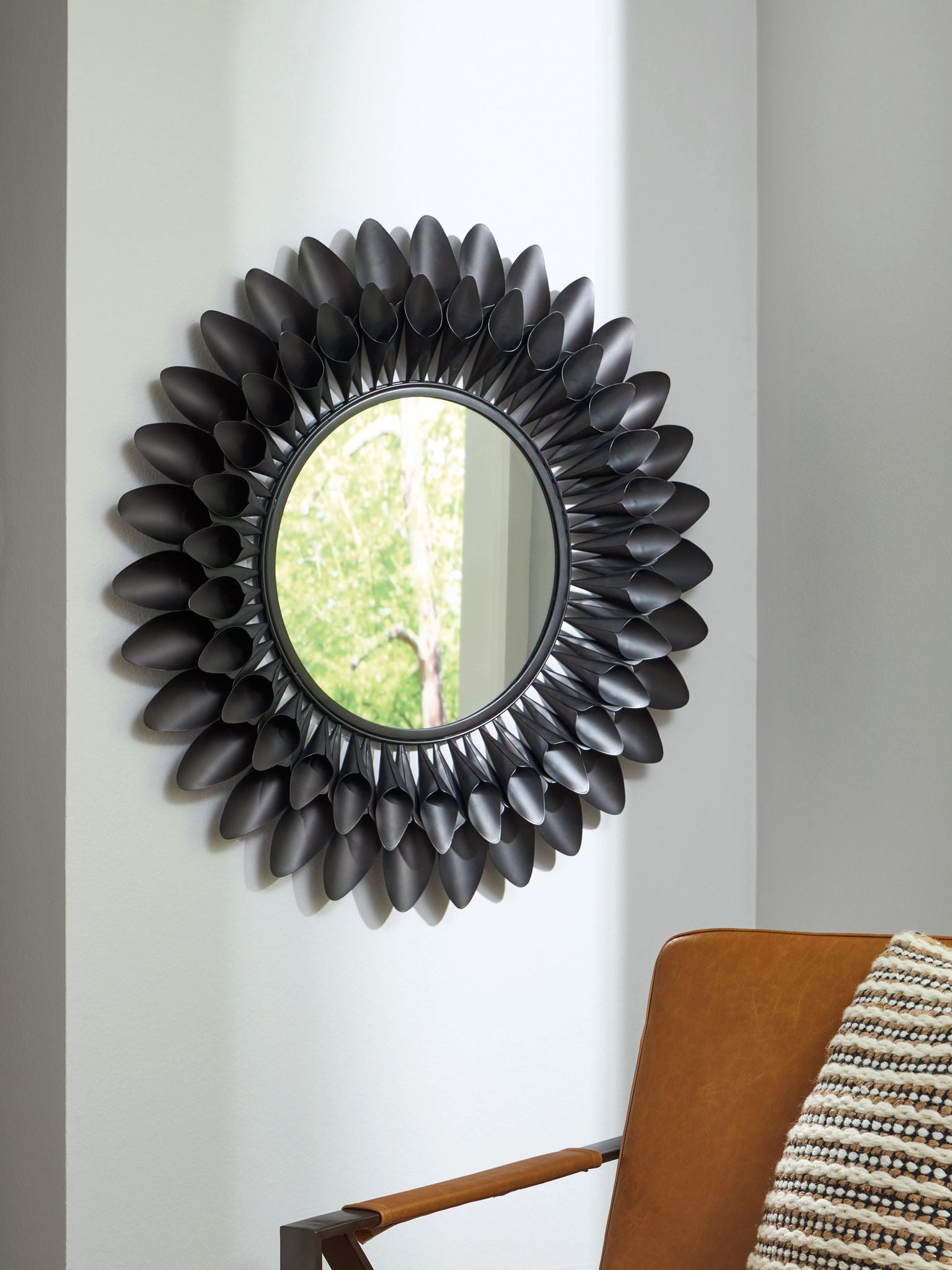Round accent mirror with dark metal petal frame, reflecting outdoor light