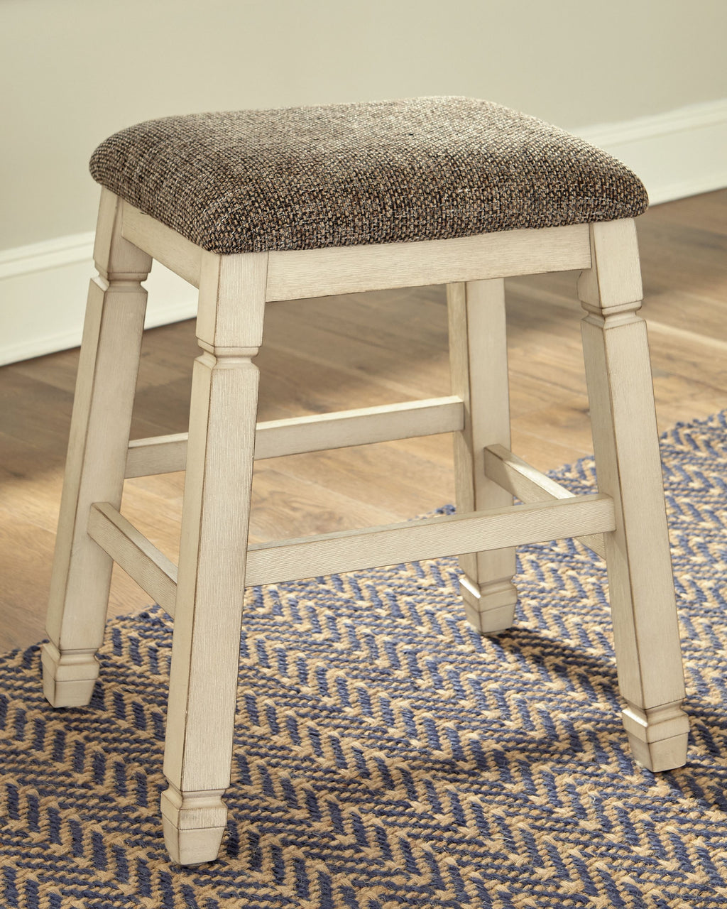 Upholstered stool with textured neutral fabric seat and light wood turned legs, open frame