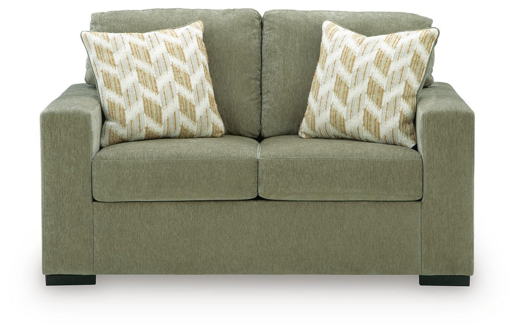Olive green upholstered loveseat with two patterned accent pillows and padded arms
