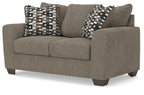 Grey suede loveseat with padded arms and two patterned throw pillows