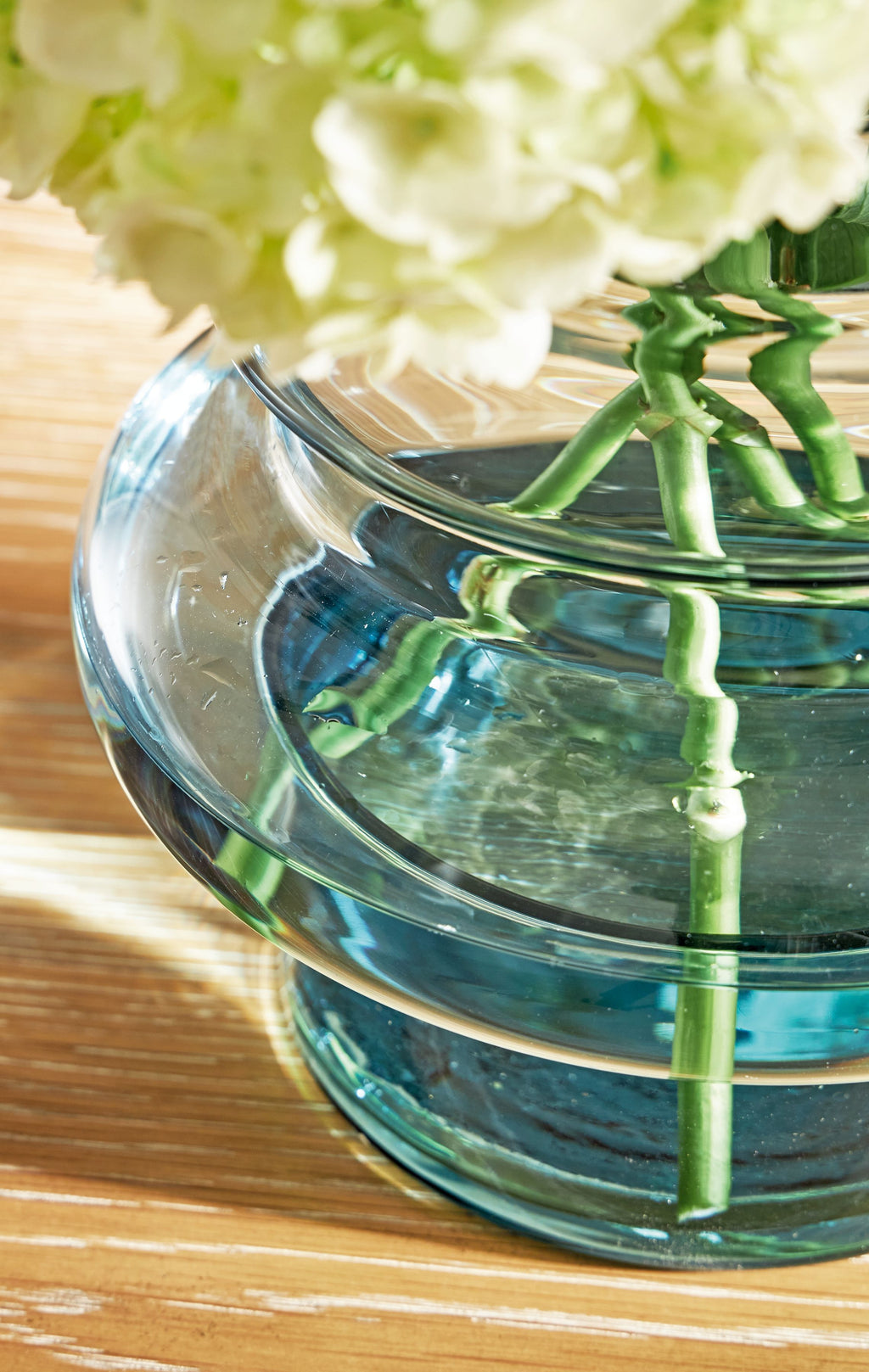 Blue glass vase with green stems and white flowers, side view