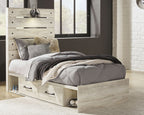 Light wood panel bed with two side drawers and gray bedding with patterned throw and pillows