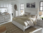 White panel bed with beige bedding and two nightstands, with dresser and mirror nearby