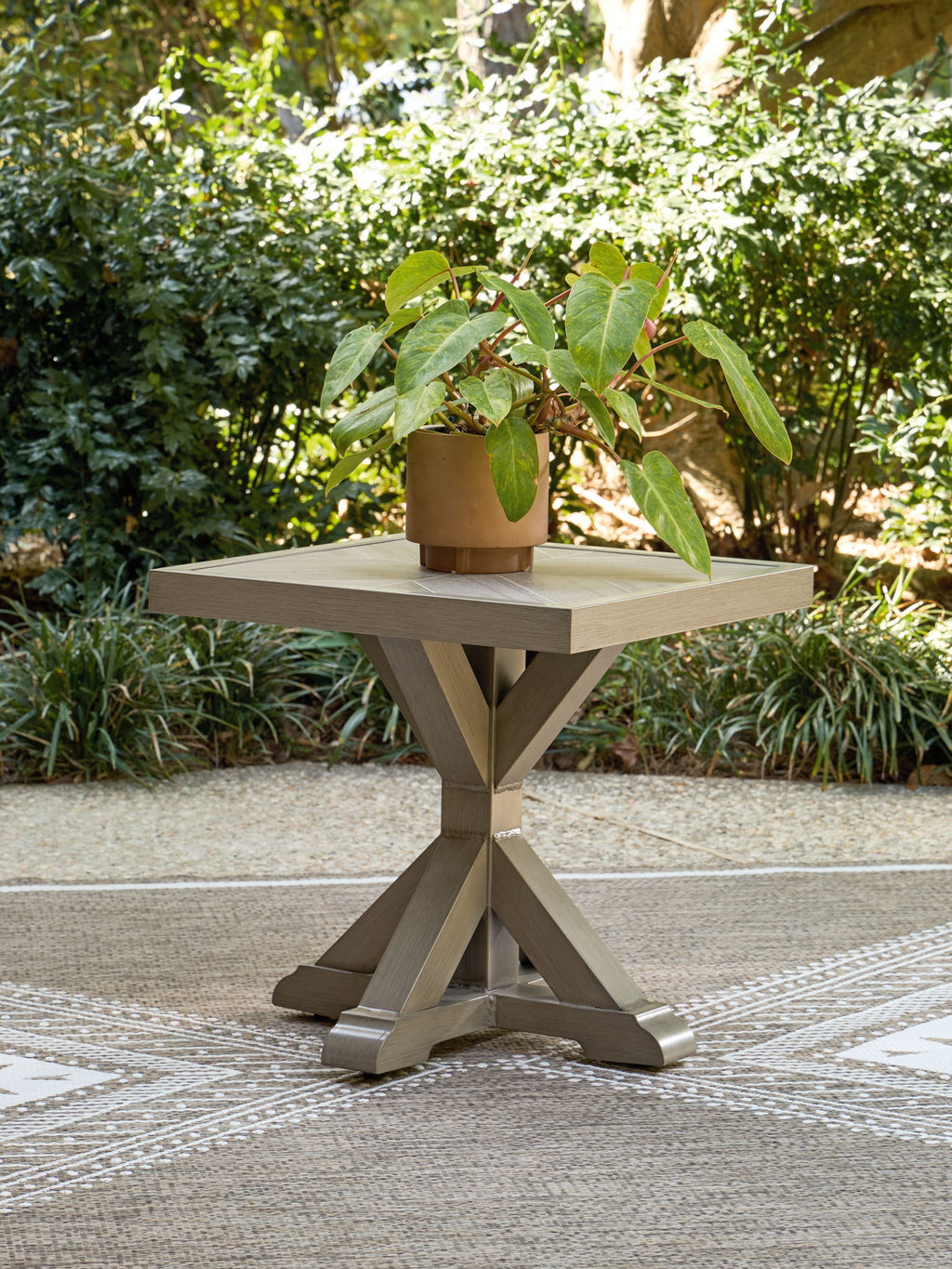 Beige square end table outdoors with tabletop planter holding a pot of greenery
