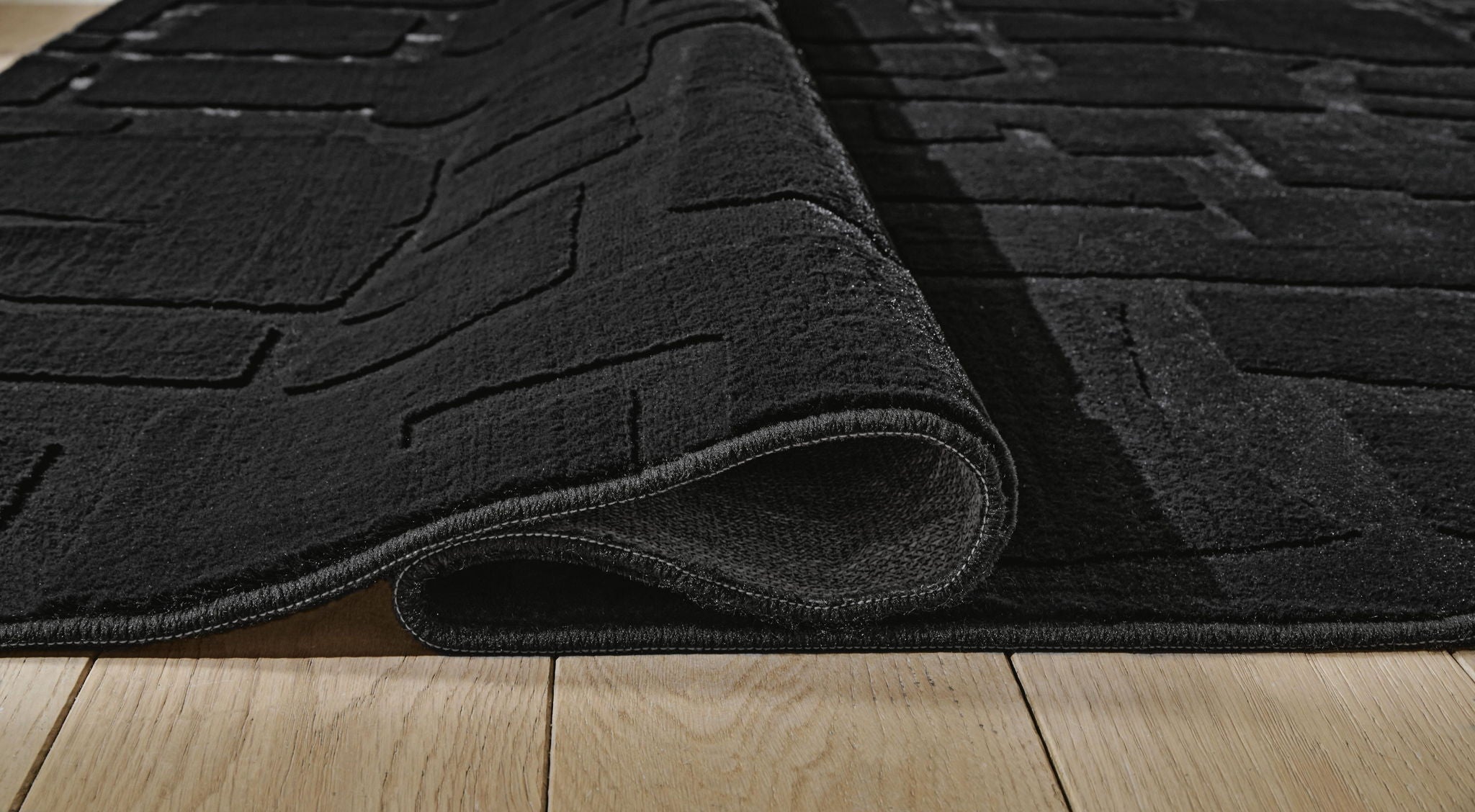 Washable rug close-up, black brick-pattern texture with rolled edge