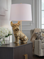 Gold dog table lamp with white fabric drum shade on dark table