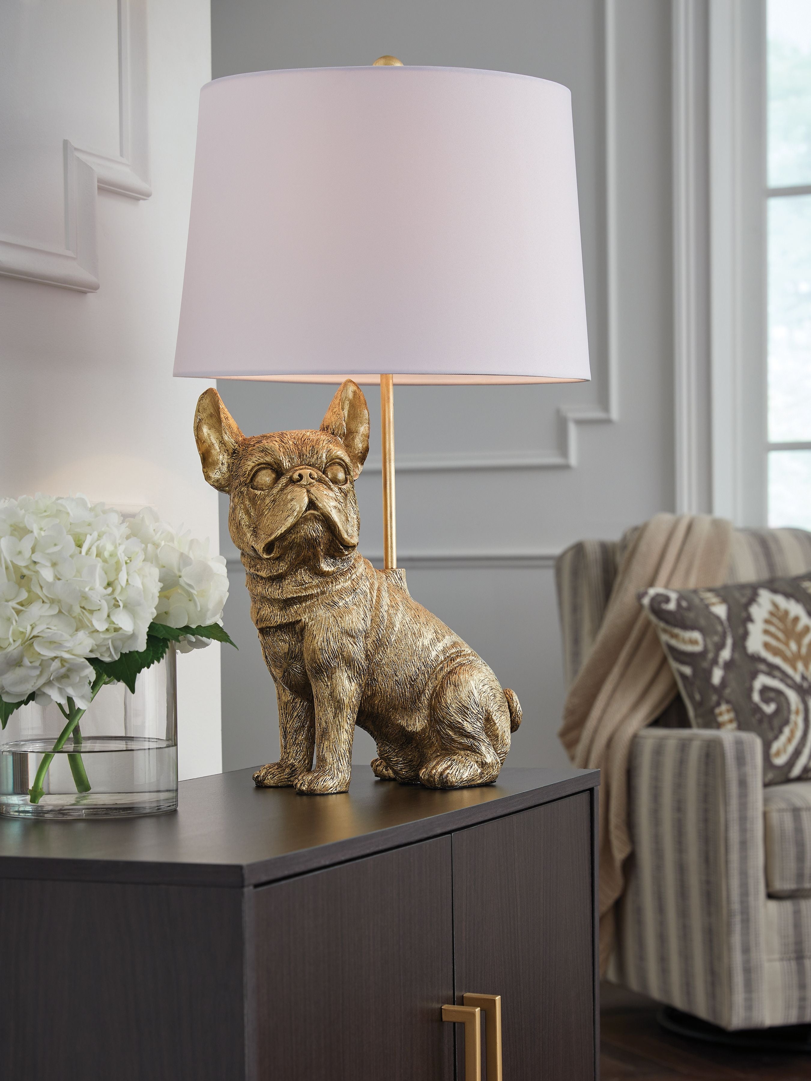 Gold dog table lamp with white fabric drum shade on dark table