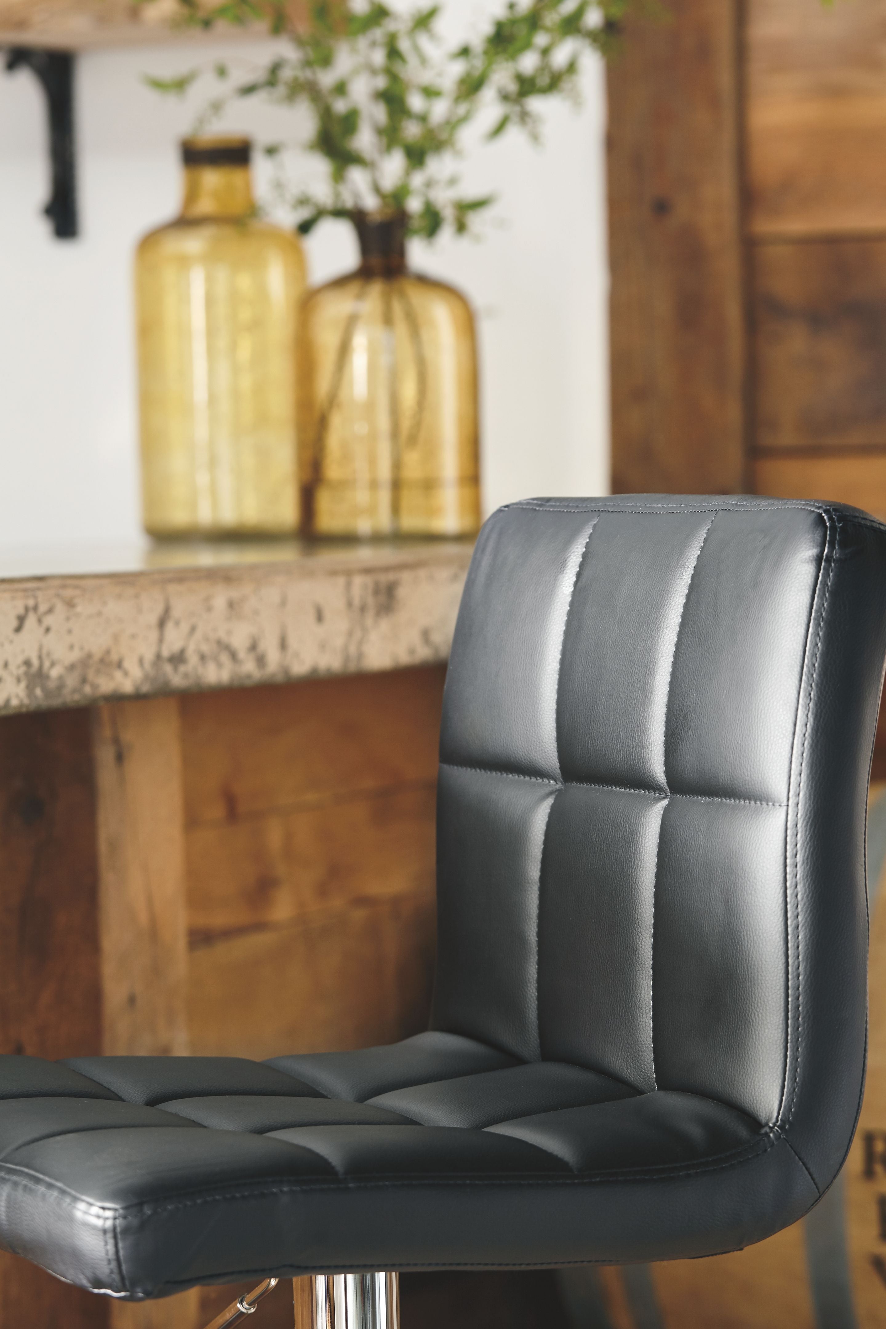 Black barstool with padded leather-look seat and tall back, chrome height stem visible