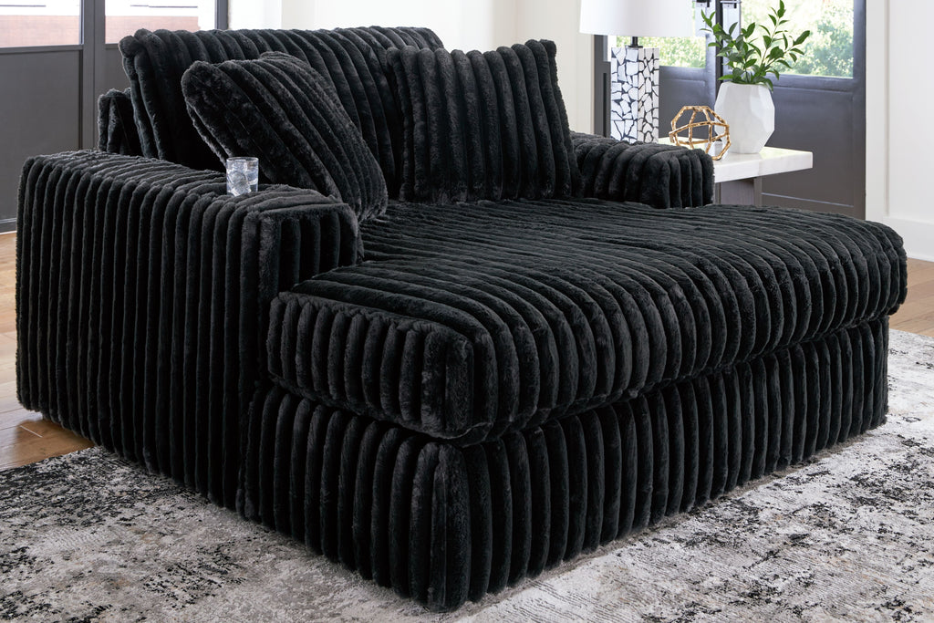 Oversized chaise with ribbed black fabric upholstery and wide track-style seat.