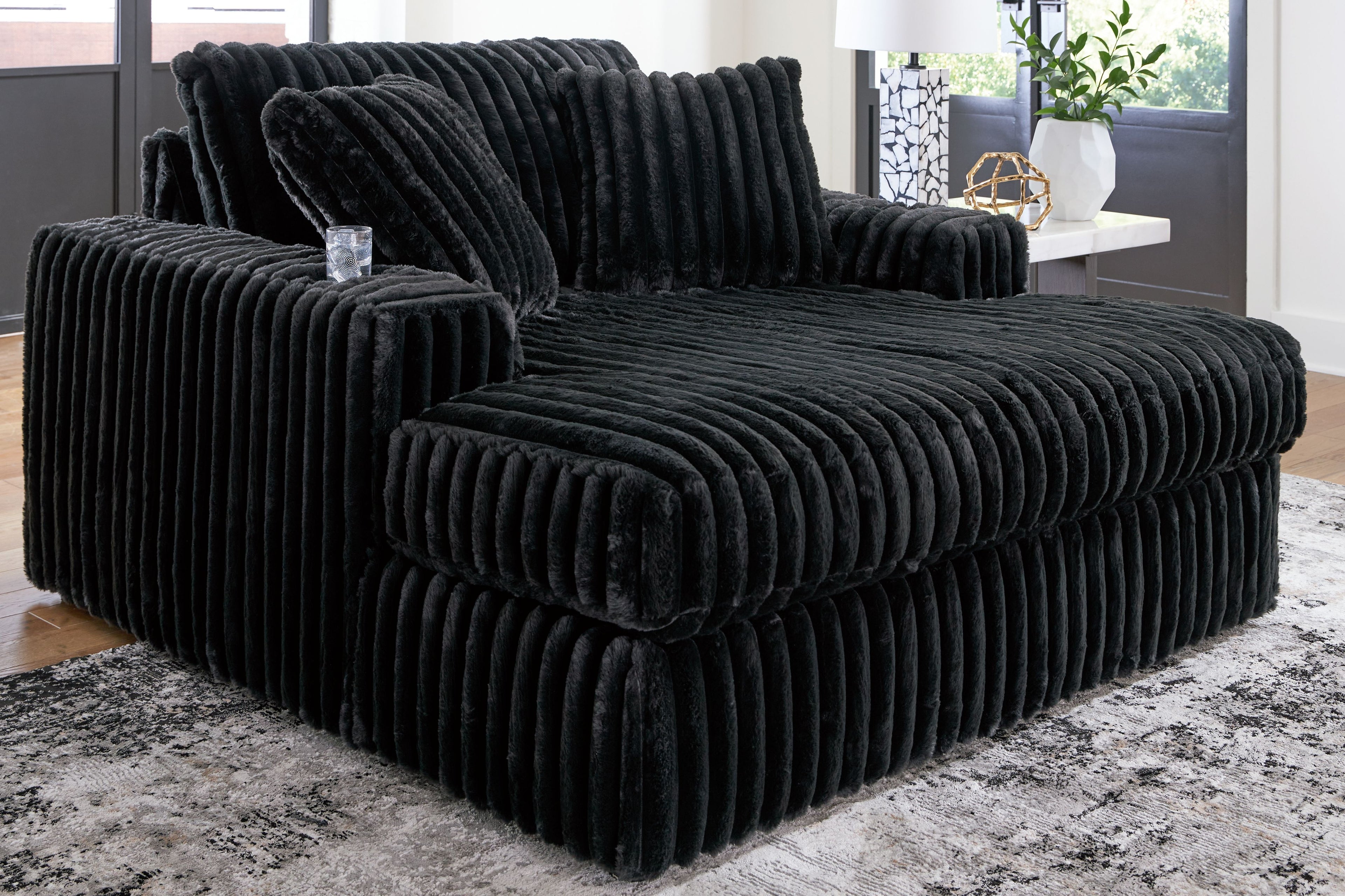 Oversized chaise with ribbed black fabric upholstery and wide track-style seat.
