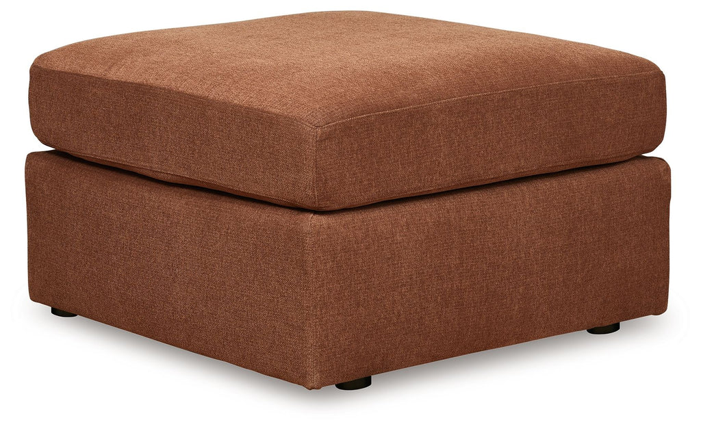 Light brown accent ottoman with cushioned top and two-tier square base, black feet.