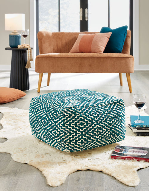 Teal and ivory geometric pouf shown in a living room, rounded top seat.