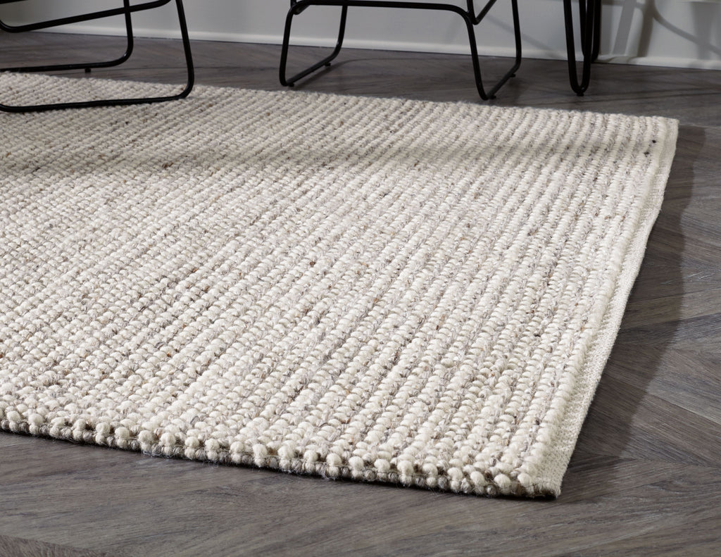 Beige woven rug with low loop pile and stitched border, corner view