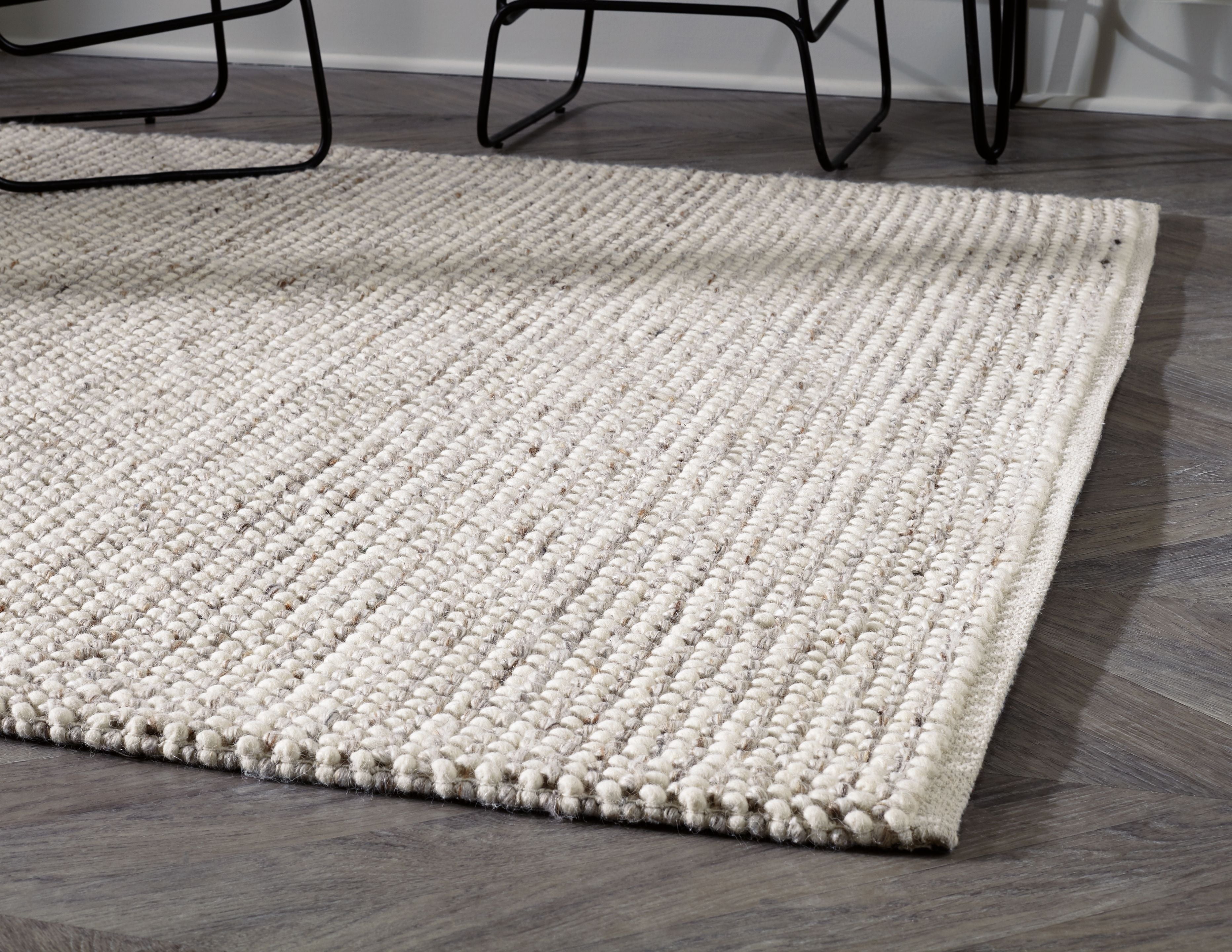 Beige woven rug with low loop pile and stitched border, corner view